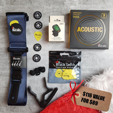 BlackSmith navy blue guitar strap, yellow guitar picks, 3 pack of 11/52 strings, Aroma digital chromatic tuner, BlackSmith strap locks, black capo and a Christmas stocking on a grey background. Tag says '$116 value for $89" 