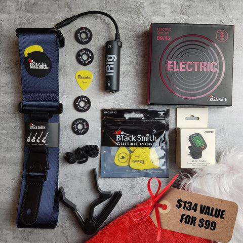 BlackSmith navy blue guitar strap, yellow guitar picks, 3 pack of 09/42 strings, Aroma digital chromatic tuner, BlackSmith strap locks, black capo, iRig and a Christmas stocking on a grey background. Tag says '$134 value for $99" 