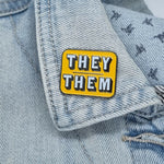 Yellow They Them pronoun pin on collar of denim jacket