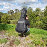 Man squatting down while wearing CRSG206CBK Crossrock classical guitar gig bag